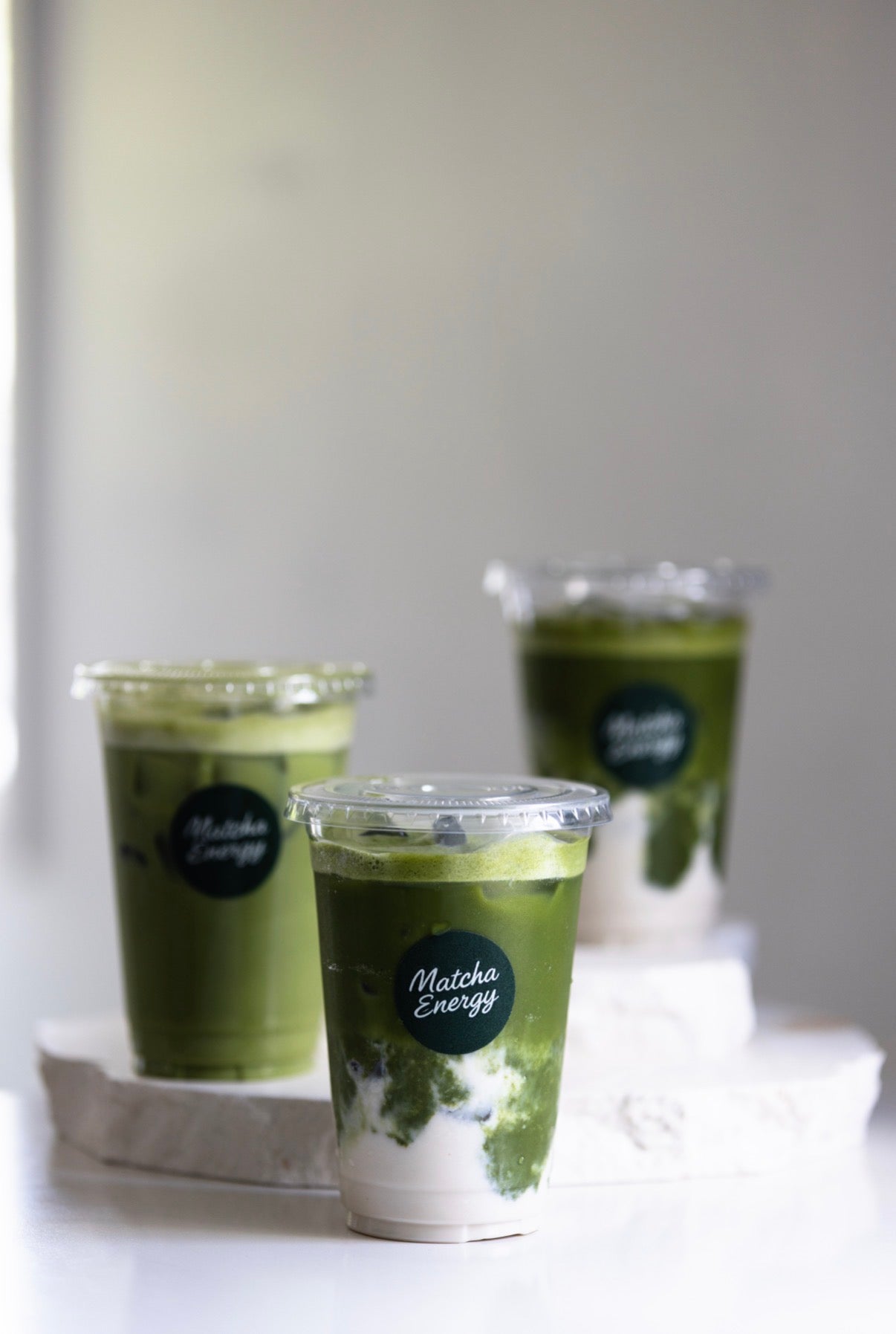 Three matcha drinks in plastic cups with 'Matcha Energy' label on a white surface.