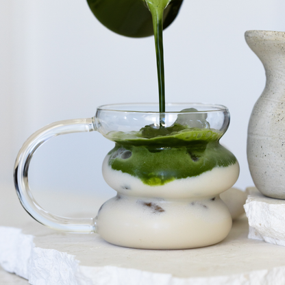 Matcha Energy being poured into a glass coup with a white base on a light background